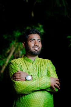 Confident man in traditional green outfit posing outdoors at night, expressing joy.