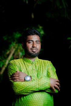 Casual portrait of a man wearing green traditional attire, standing outdoors at night.