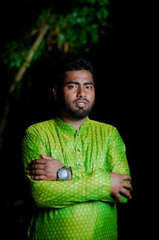 A man in bright green traditional attire posing confidently outdoors at night.