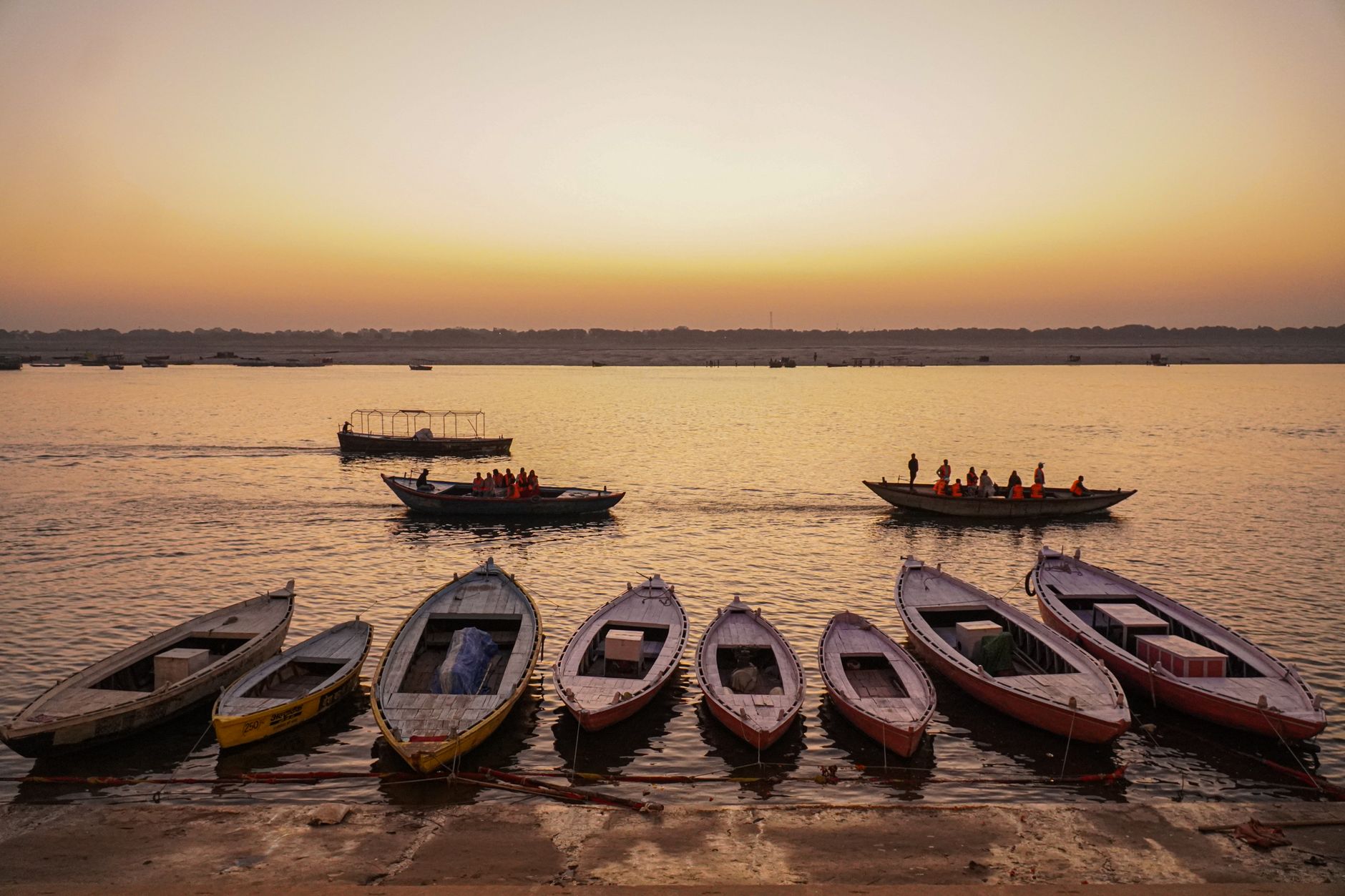 sunrise over the Ganges in Varanasi, boats drifting beside ancient ghats and softly glowing temple architecture
