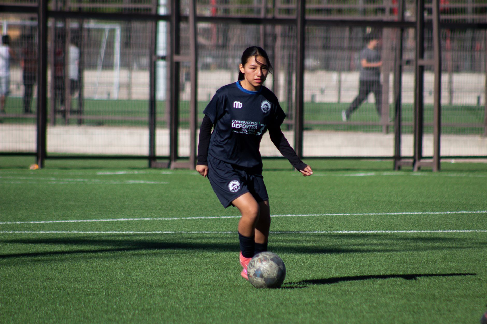 A young female athlete playing soccer on a green outdoor field during the day.