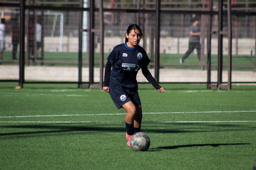 A young female athlete playing soccer on a green outdoor field during the day.