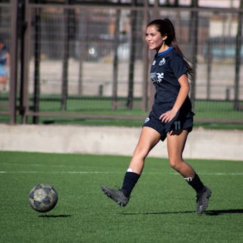 Young female athlete in blue soccer uniform dribbling a soccer ball outdoors on a sunny day.