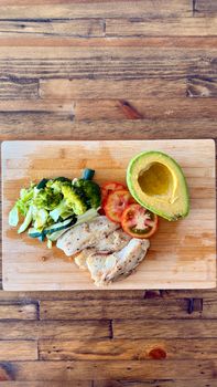 Delicious chicken with fresh vegetables and avocado on a wooden table.