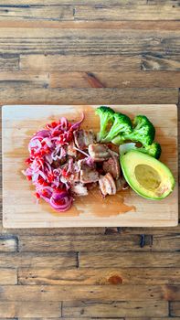 Delicious chicken with broccoli, avocado, and pickled onions on a wooden board.