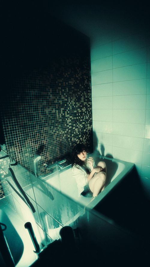 Free Woman in bathtub with dark tiles creating a dramatic and moody atmosphere. Stock Photo