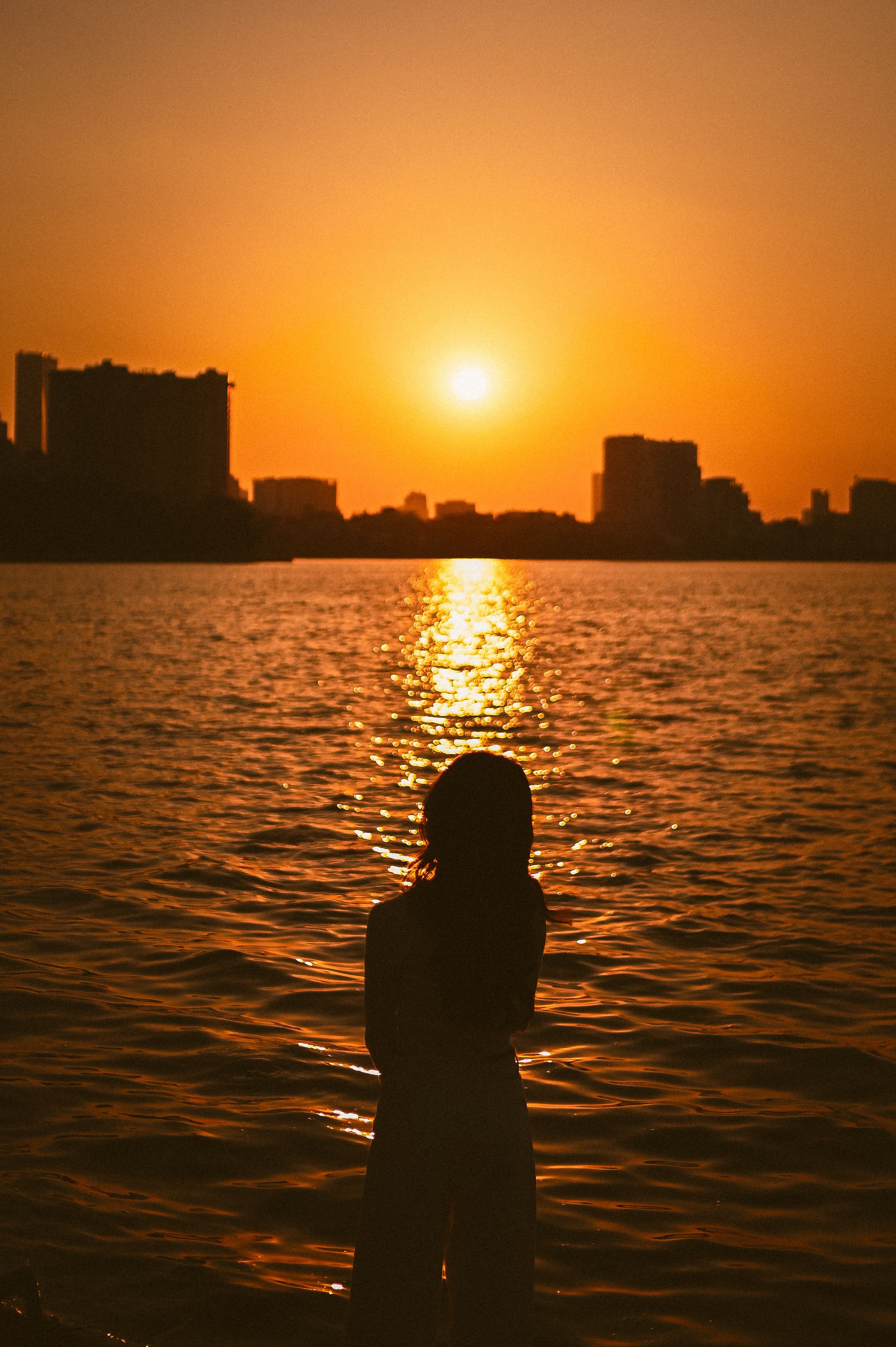 A person silhouetted against a vibrant sunset over a tranquil body of water.