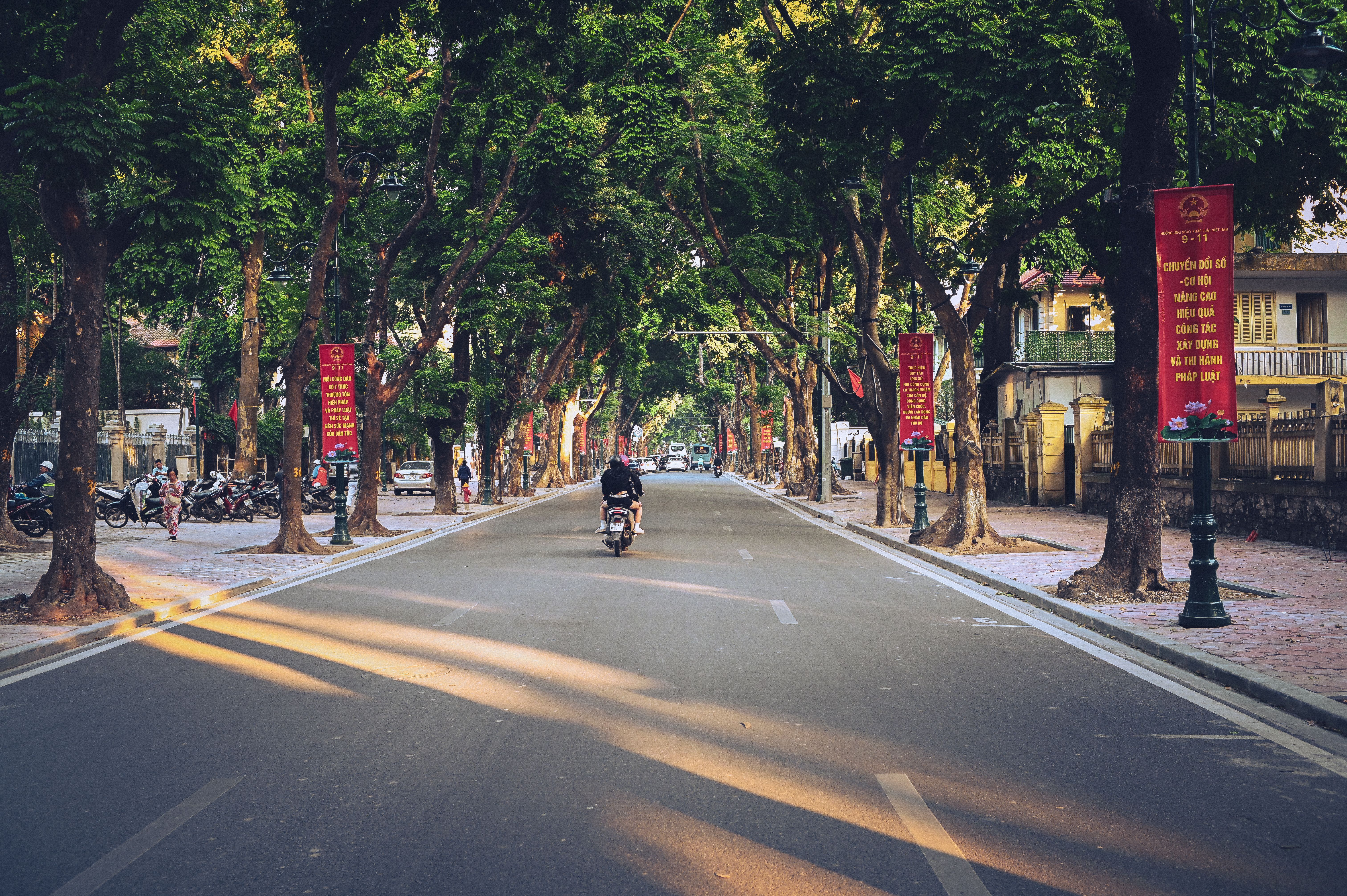 A quiet rural alley in Vietnam with a fenced compound, parked motorbikes, and late-evening activity
