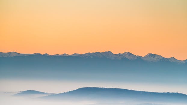 A peaceful view of misty mountains during sunrise with soft pastel colors.