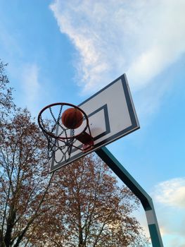 Basketball scoring a swish on an outdoor hoop under a clear sky.