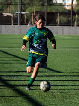 Teen athlete dribbling soccer ball on outdoor field during daytime match.