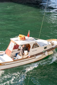 A man navigating a small fishing boat on clear green water in bright sunlight.