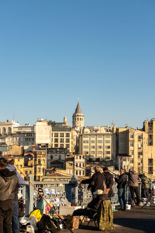 Free Fishermen gather on Istanbul's Galata Bridge with the iconic Galata Tower in the backdrop, under a clear blue sky. Stock Photo