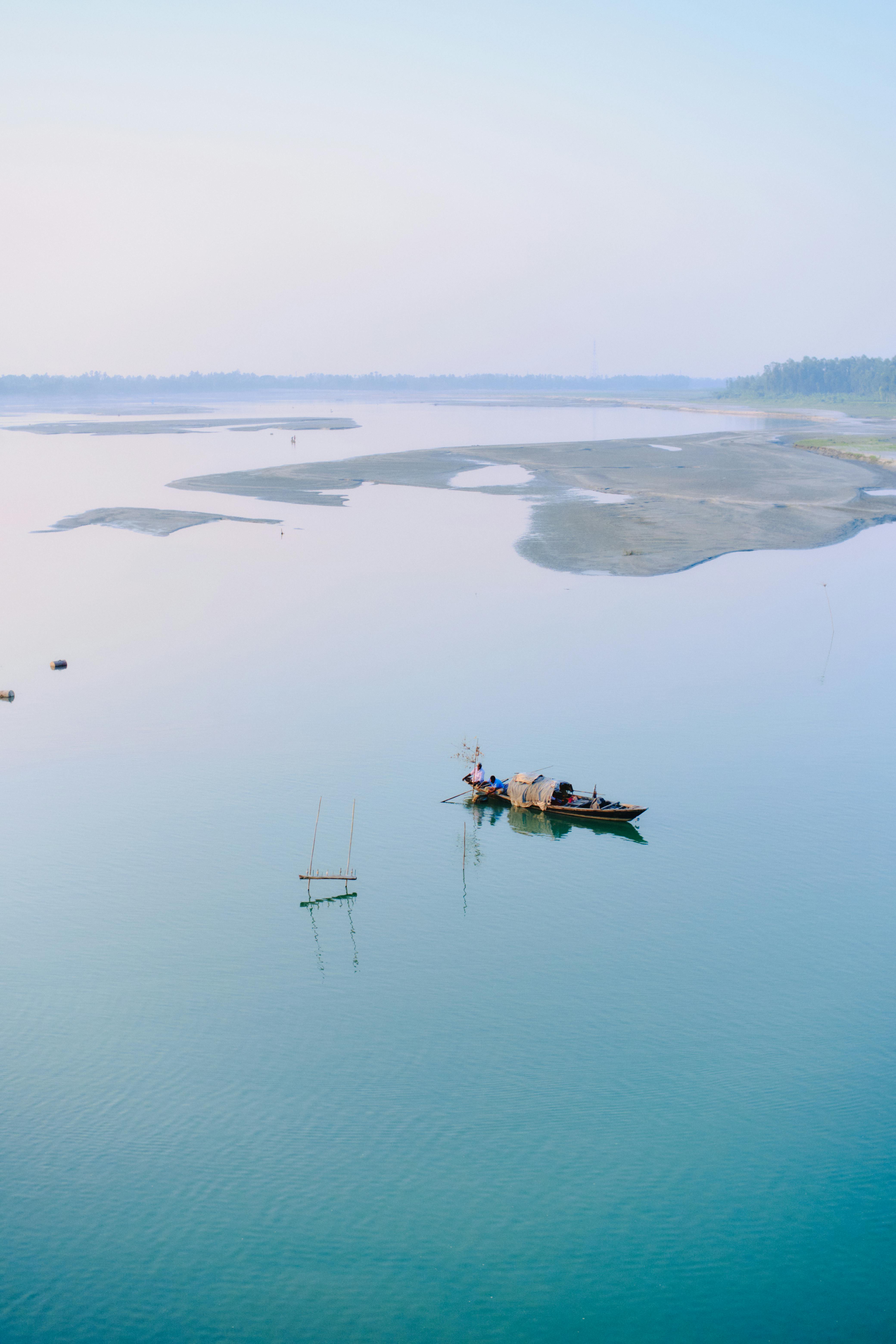 A tranquil scene of a boat on a calm river in Kurigram, Bangladesh, under a clear blue sky.