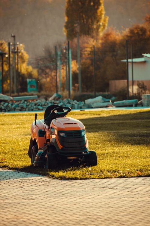 Free Vibrant orange lawn mower parked on a sunlit lawn during a beautiful autumn afternoon. Stock Photo