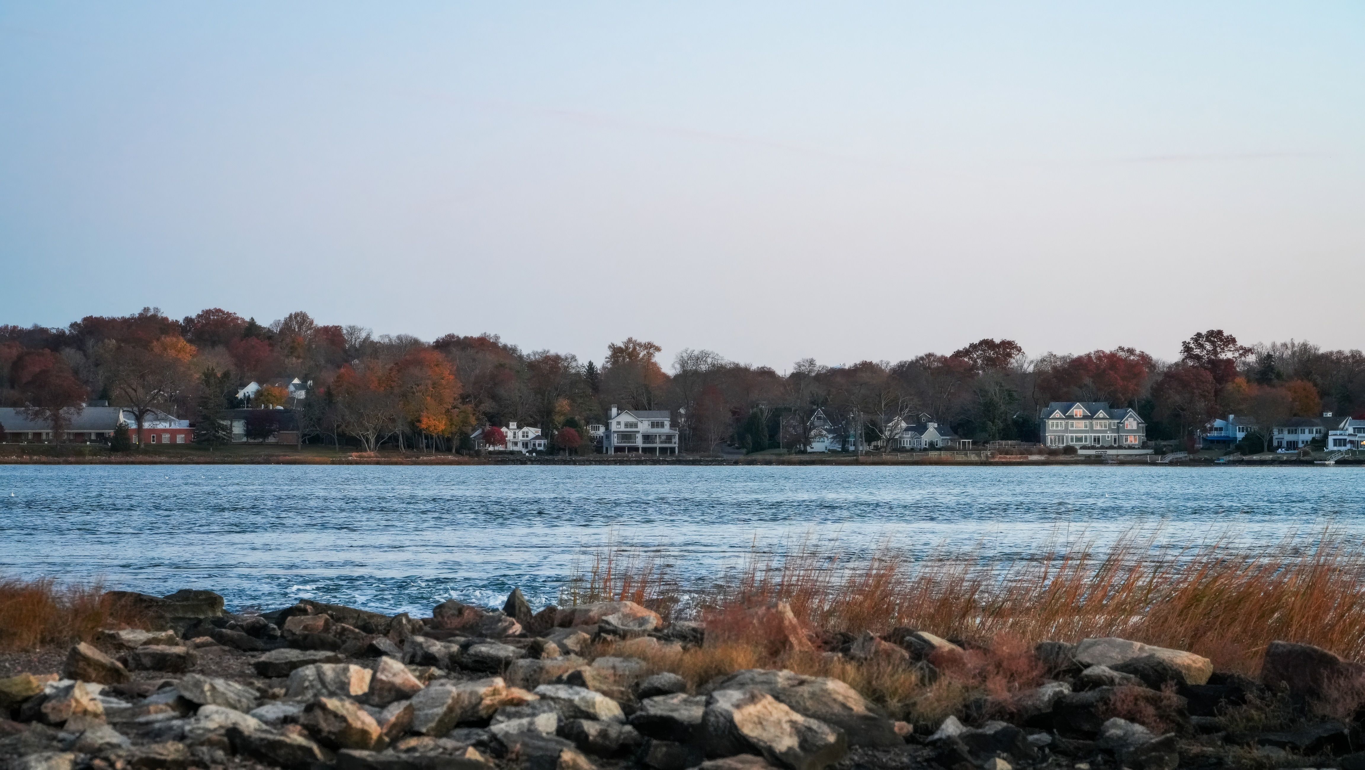 Peaceful autumn landscape by the lake with houses and colorful trees.