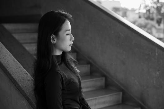 Thoughtful woman with closed eyes leaned against a staircase railing in monochrome.