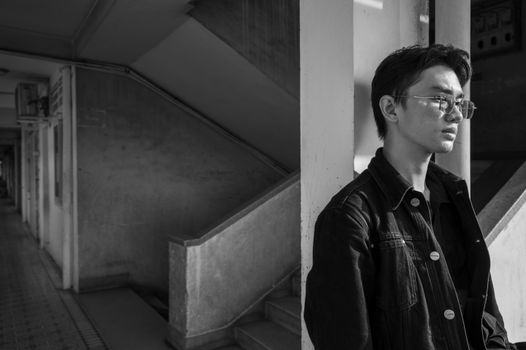 Black and white portrait of a young man in urban environment, reflecting deep thought.