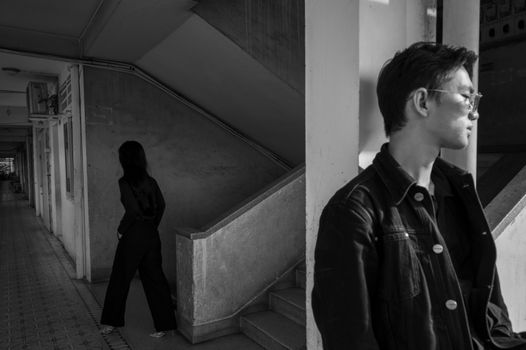 Moody black and white scene with two individuals in an indoor, urban setting.