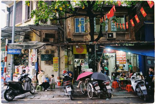 Free Vibrant street life in Hanoi, showing locals at a food stand with motorbikes and city life. Stock Photo