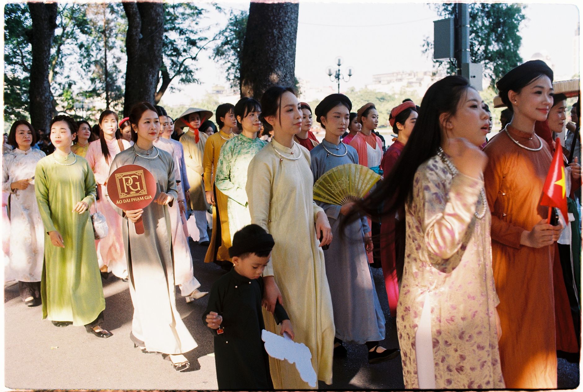 A vibrant parade of women in traditional Ao Dai dresses during an outdoor cultural event.