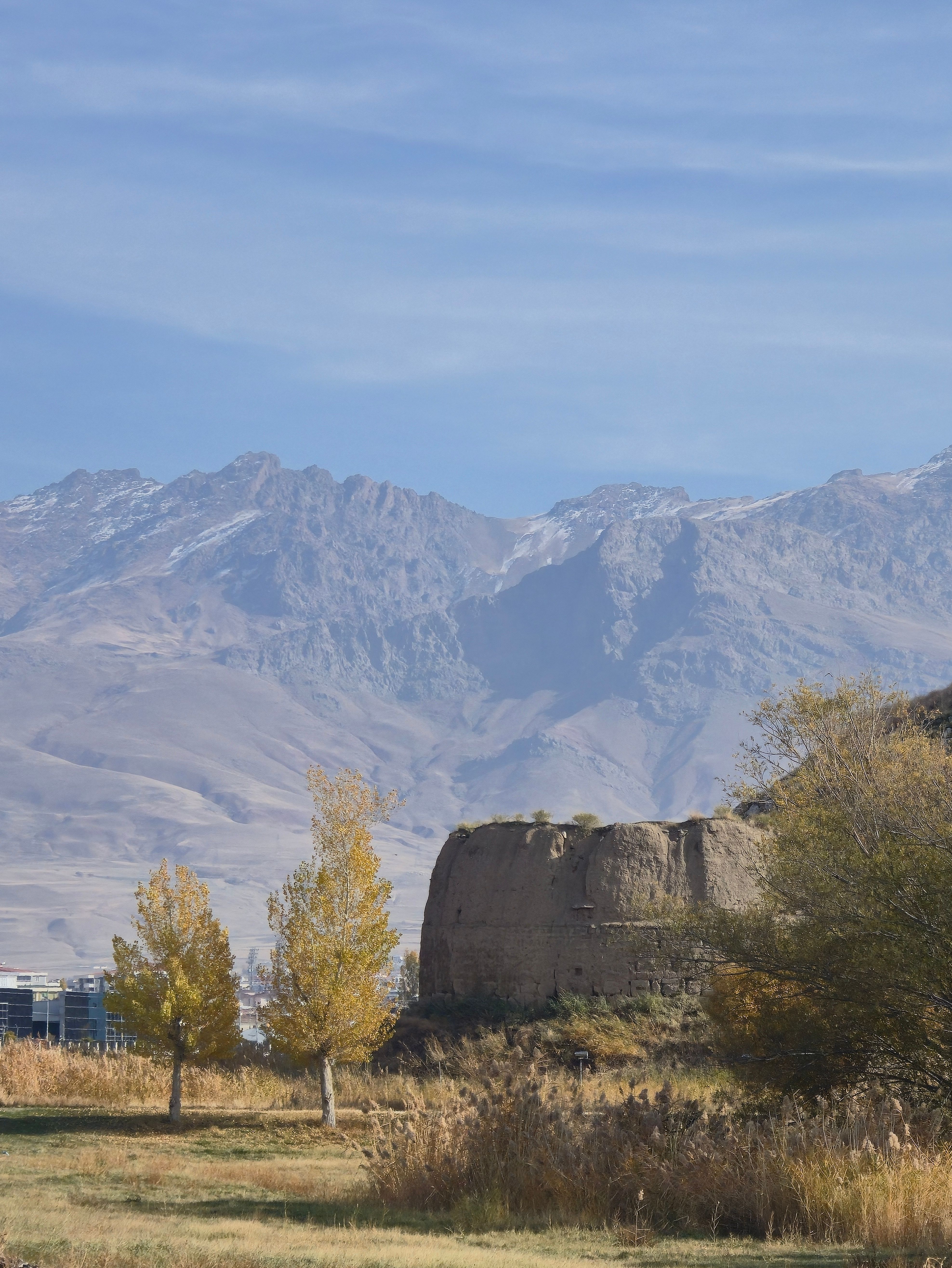 A historic tower set against snow-capped mountains under a clear sky, showcasing natural beauty.