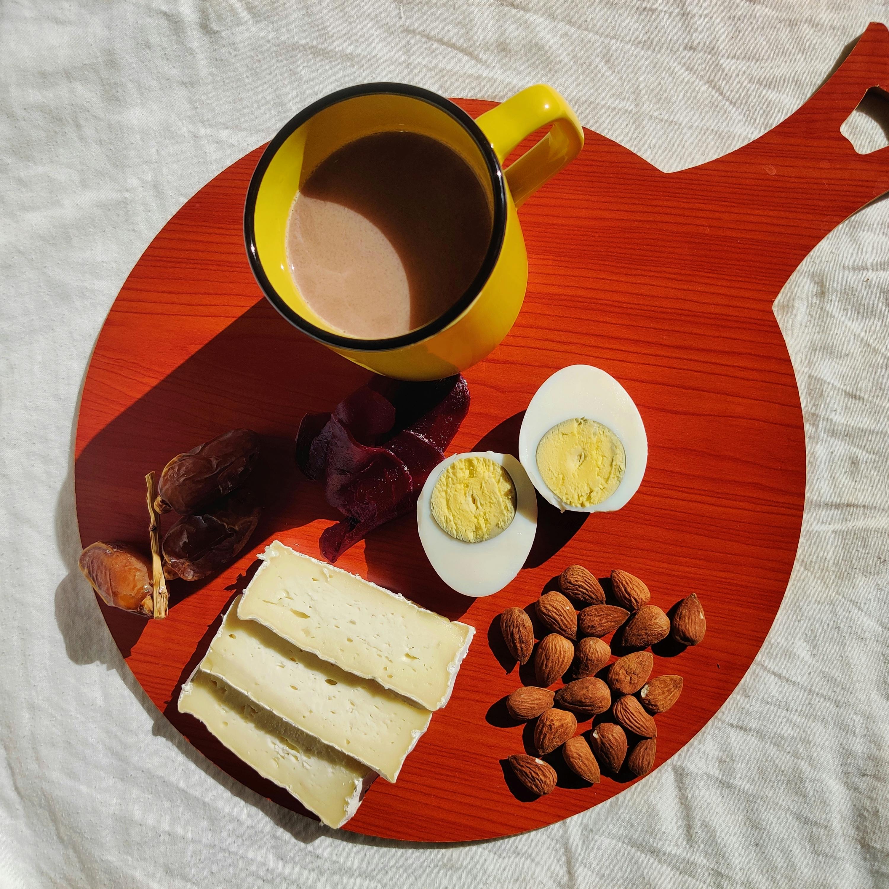 A vibrant Algerian breakfast featuring cheese, boiled egg, almonds, and coffee on a red board.