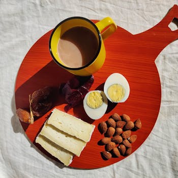 A vibrant Algerian breakfast featuring cheese, boiled egg, almonds, and coffee on a red board.