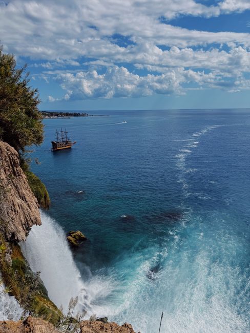 Breathtaking view of Duden Waterfalls cascading into the Mediterranean Sea with a pirate ship sailing nearby.