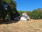 A picturesque stone chapel with rustic architecture surrounded by trees in rural Greece.