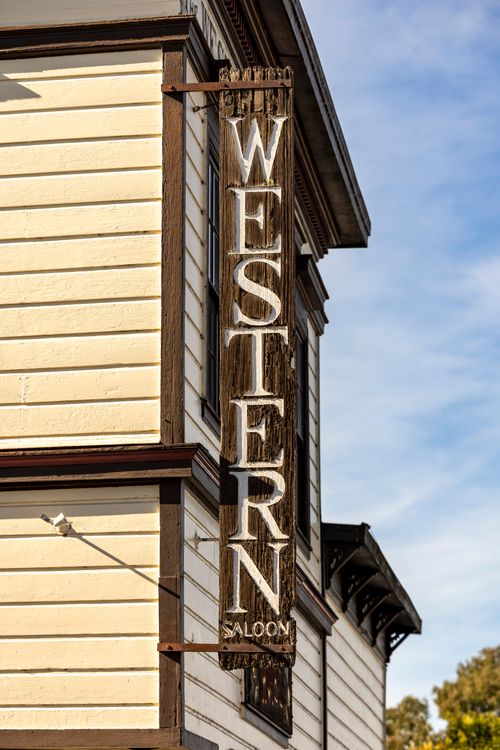Free Close-up of a vintage 'Western Saloon' sign on a historic wooden building under a blue sky. Stock Photo