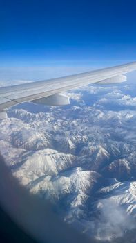 Stunning aerial view of snow-covered mountains seen from an airplane window. Clear blue sky.
