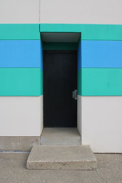 Free A minimalist entrance with bold geometric patterns and a black door set in a concrete structure. Stock Photo