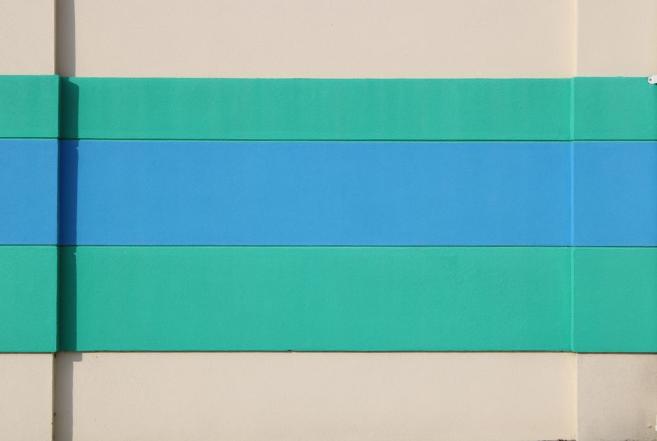 Abstract image of a wall with teal and blue horizontal stripes on a beige background.