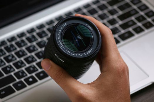 Close-up of a hand holding a Canon camera lens above a laptop keyboard.