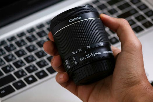 Detailed close-up of a DSLR camera lens held in hand over a laptop, showcasing photography equipment.