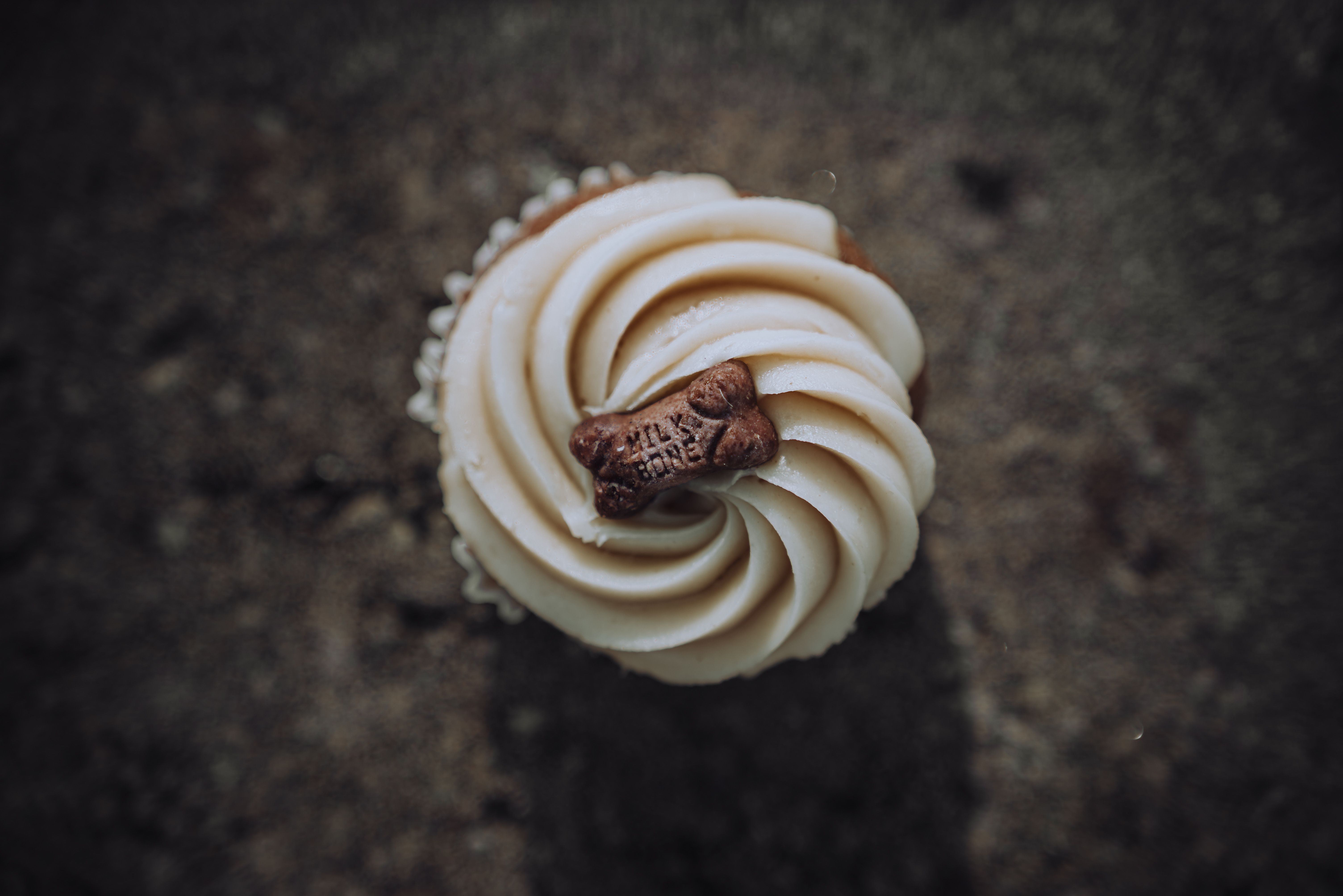 Top view of a gourmet cupcake with cream frosting and a biscuit on top.