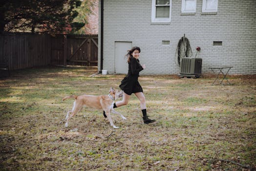 A joyful moment outdoors featuring a woman running with a dog in a backyard.