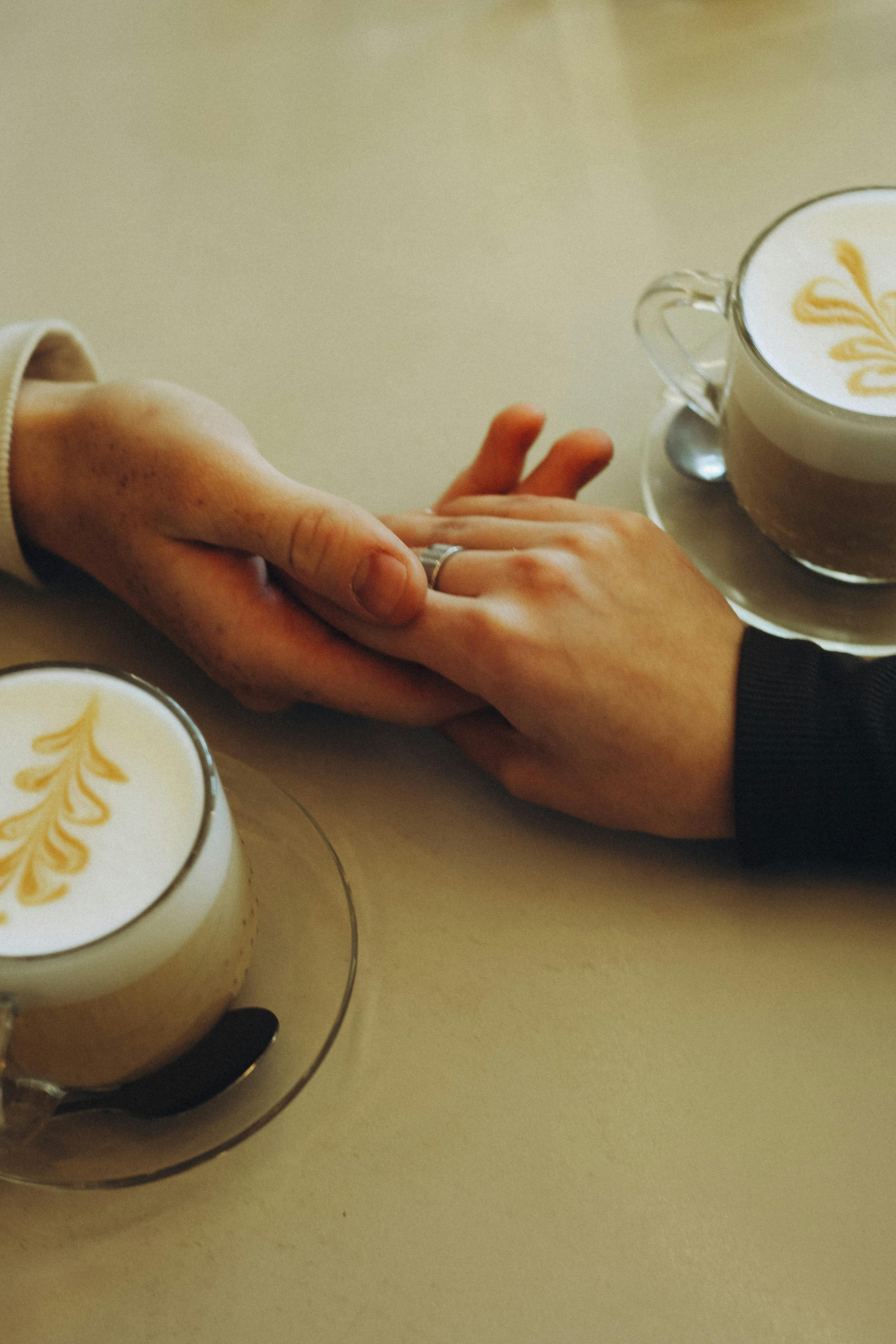 A couple holding hands over lattes with beautiful art designs in a cozy café.