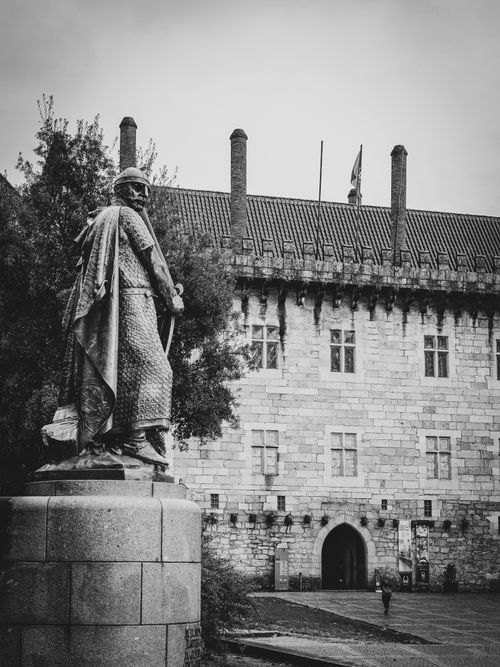 Free Black and white photo of a historical statue and medieval castle exterior. Stock Photo