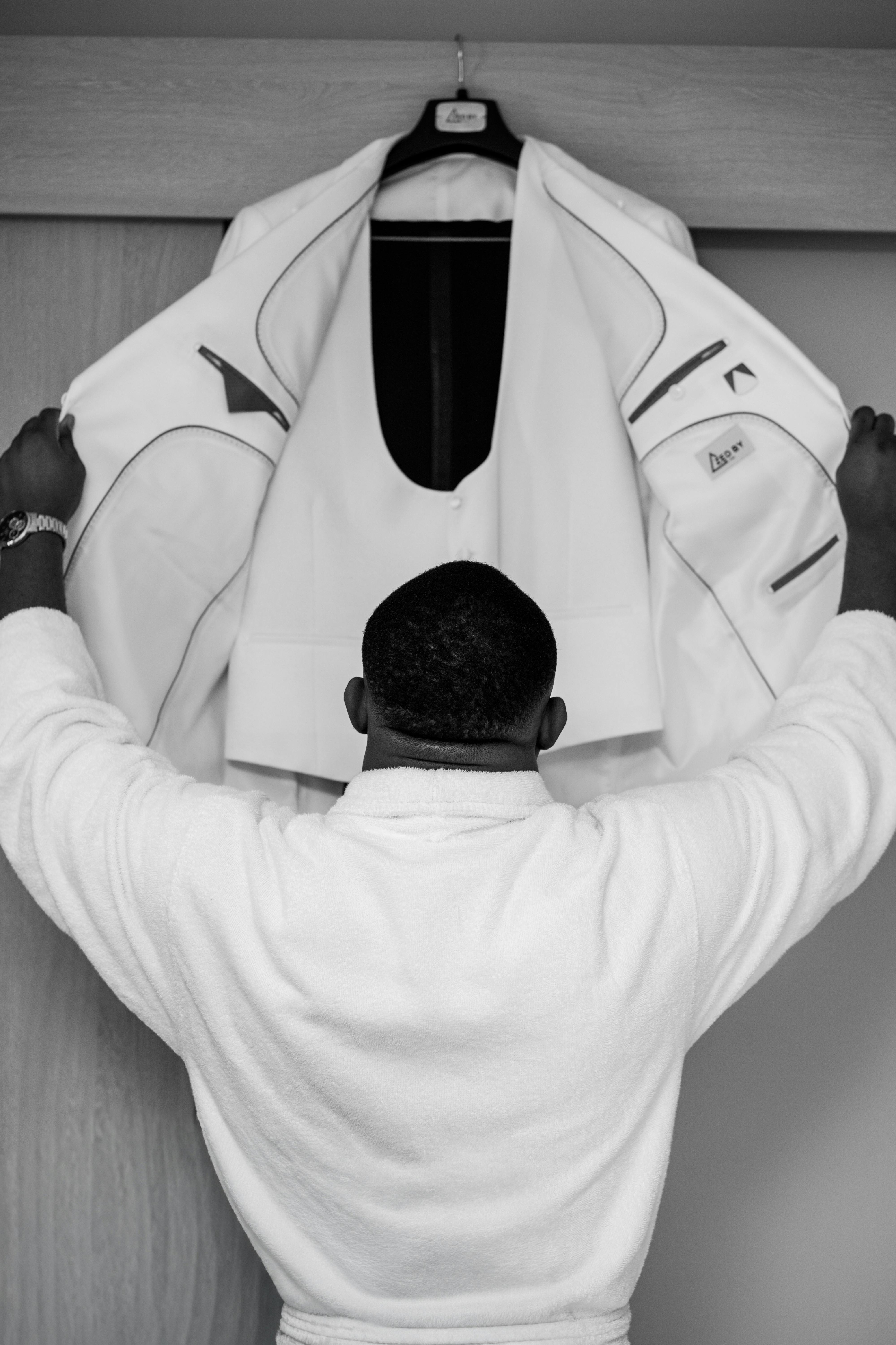 A man in a robe prepares his elegant white suit for a special occasion.