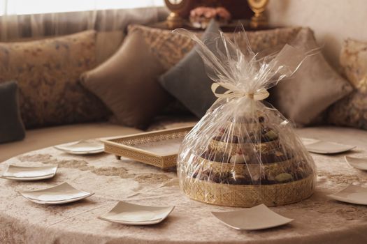 A beautifully wrapped gift tray of assorted sweets on an ornate table setting, perfect for celebrations.