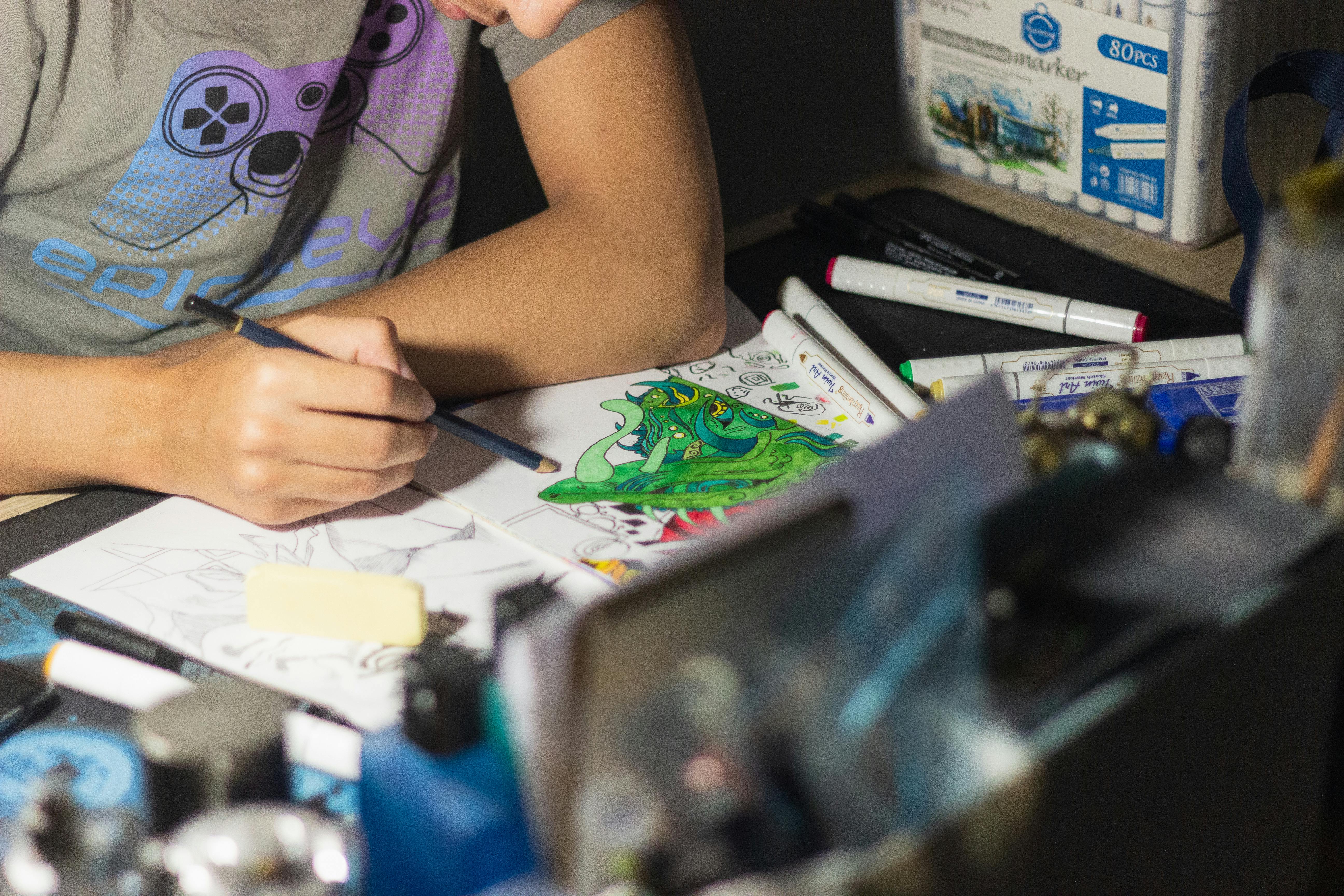Close-up of an artist sketching a vibrant illustration at a cluttered workspace.