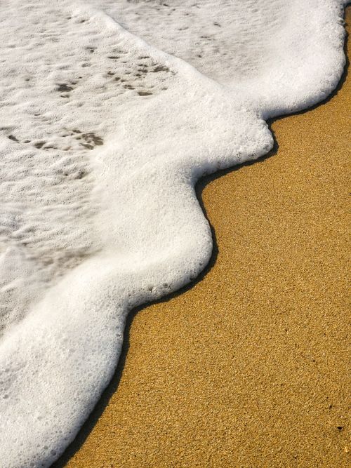 Free Close-up of ocean wave foam on golden sandy beach, capturing serene coastal beauty. Stock Photo