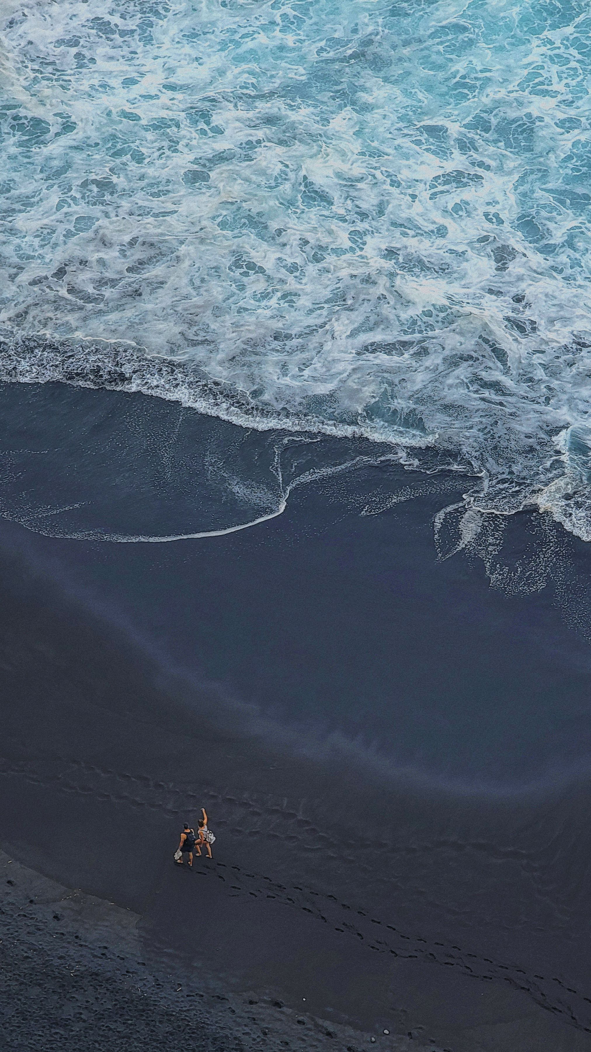 A couple strolls along a unique volcanic black sand beach with ocean waves in Tenerife, Spain.. pexels, couple, strolls