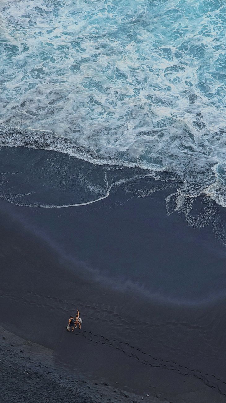 A couple strolls along a unique volcanic black sand beach with ocean waves in Tenerife, Spain.. pexels, couple, strolls