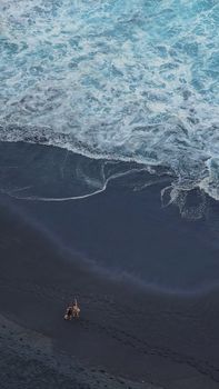 A couple strolls along a unique volcanic black sand beach with ocean waves in Tenerife, Spain.. pexels, couple, strolls