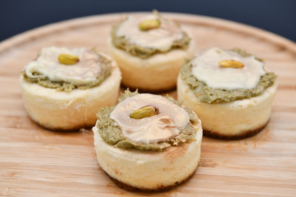 Delicious mini cheesecakes topped with pistachio cream on a wooden board.