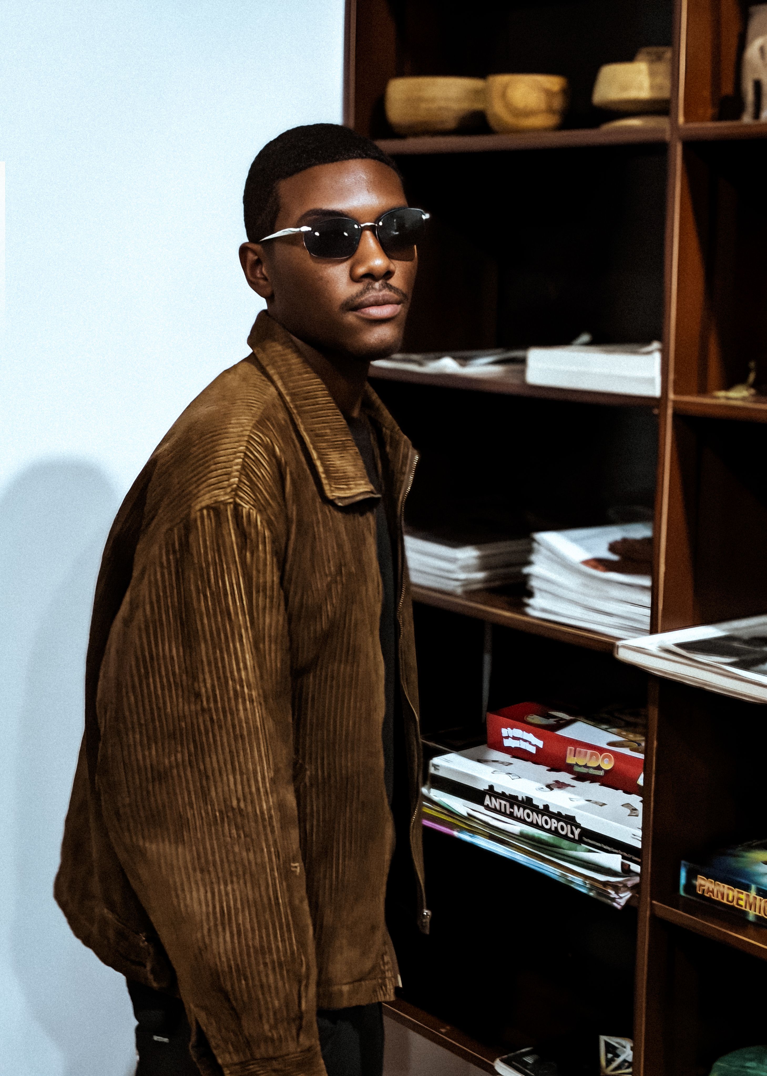Young man in sunglasses and a brown jacket posing indoors. Fashionable and modern vibe.