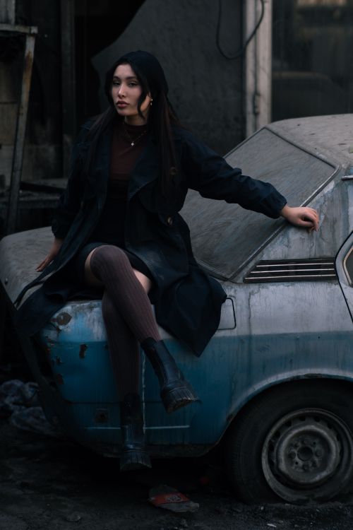 Free Woman in dark clothing sitting on an old car, creating a moody urban vibe. Stock Photo